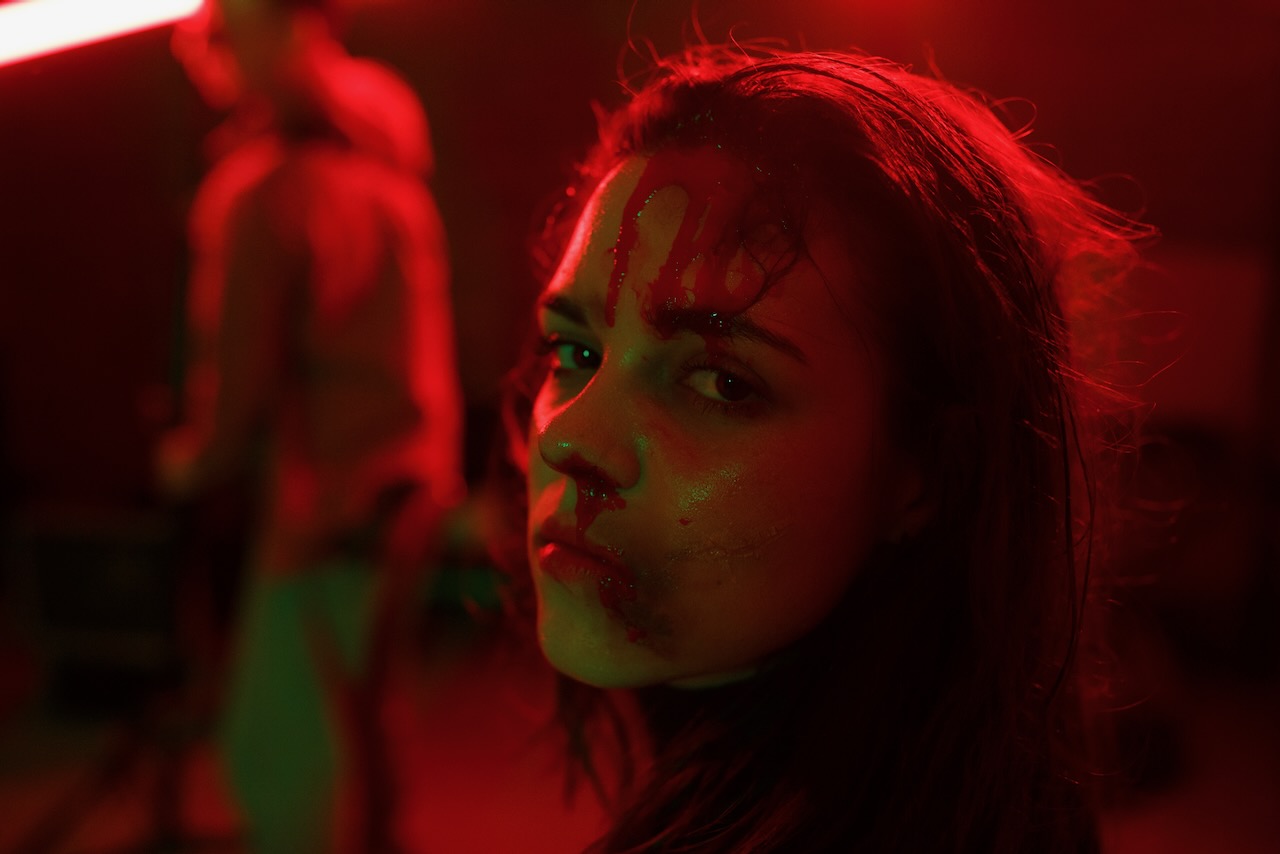 The same actress with stage blood, in red light.